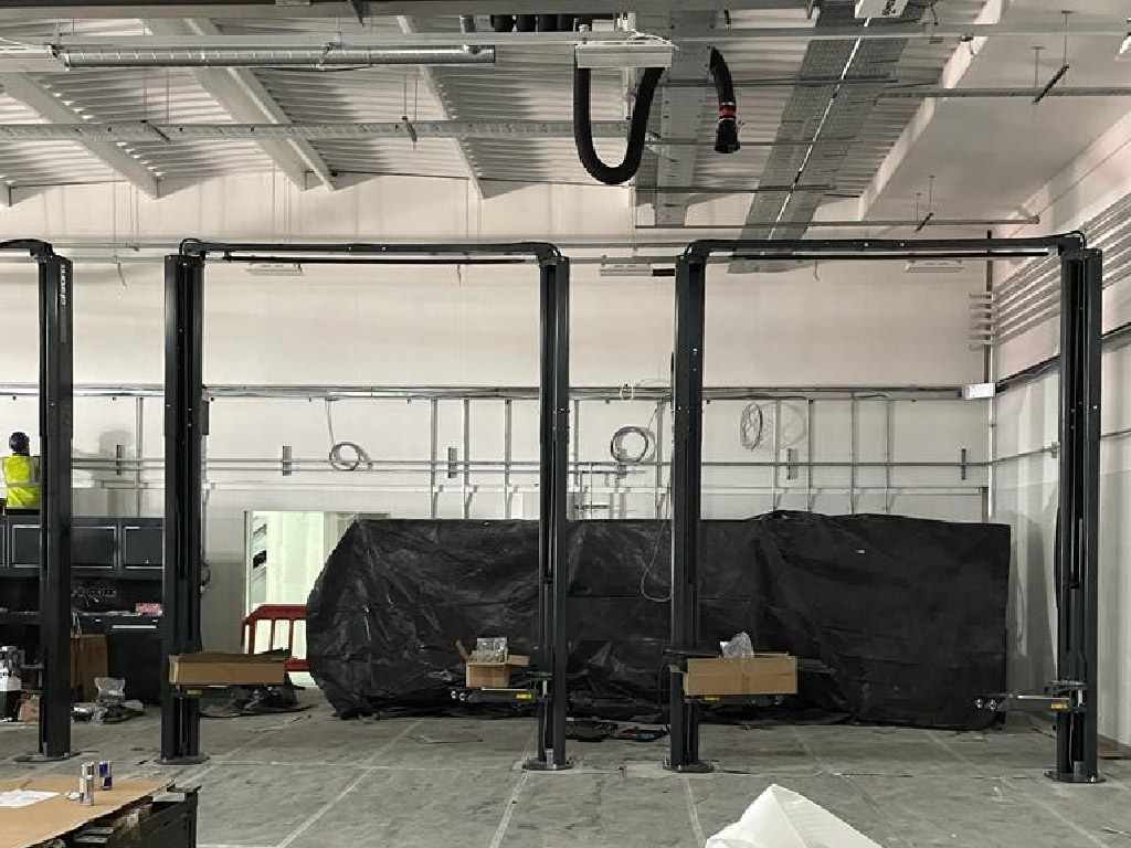 New fixed 2-post vehicle servicing lifts during installation. Base frame-free lifts offer excellent capacity and reliability, with overhead risers for power making the most of the workshop's height and avoiding the need for underground cabling between posts.