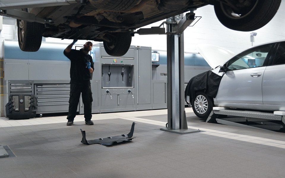 Fixed 2-post vehicle lift with vehicle lifted, next to scissor lift in use for wheel alignment work. Garage equipment installation by CCS Garage Equipment for Volkswagen Battersea, London