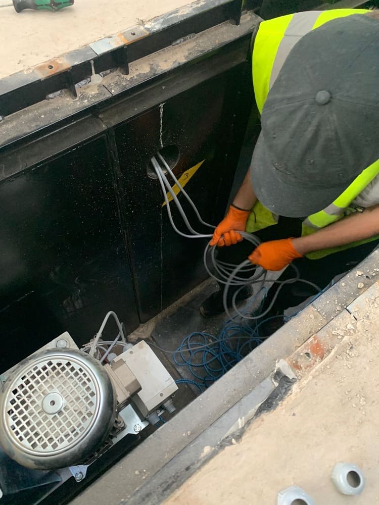 Specialist vehicle lift installation engineers positioning lift cabling